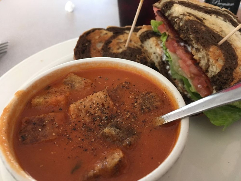 Tomato soup served with a sandwich on a table at a cozy cafe setting.