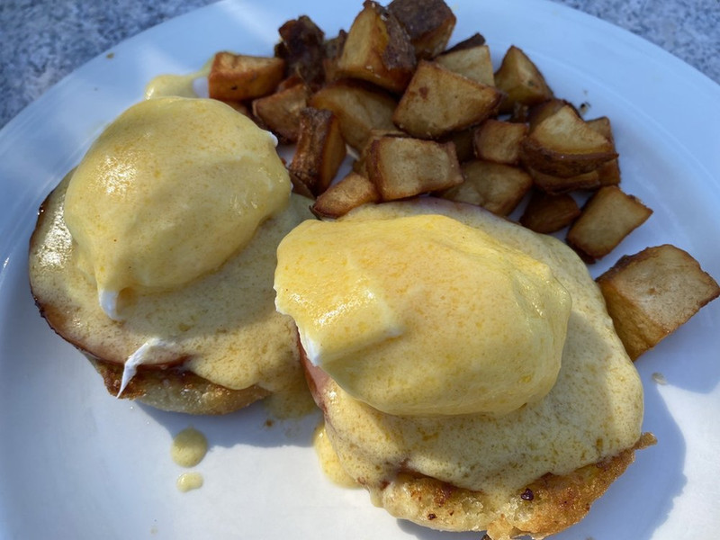 A plate featuring eggs benedict topped with hollandaise sauce, accompanied by golden, crispy potatoes.