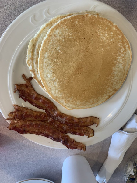 A plate of fluffy pancakes topped with syrup and crispy bacon served on a wooden table.