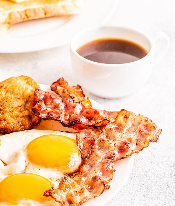 Breakfast plate featuring scrambled eggs, crispy bacon, and golden toast arranged appetizingly.